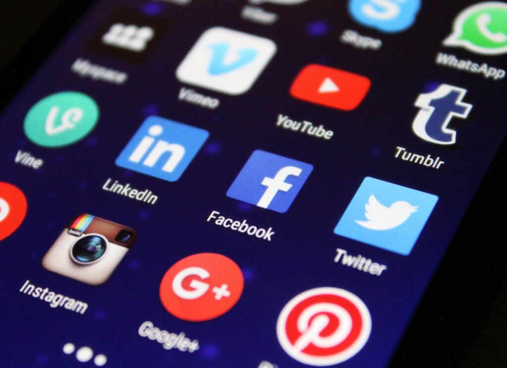 This image displays a close-up view of a smartphone screen featuring popular social media app icons, including Facebook, Twitter, Instagram, LinkedIn, and YouTube, among others, set against a dark background.