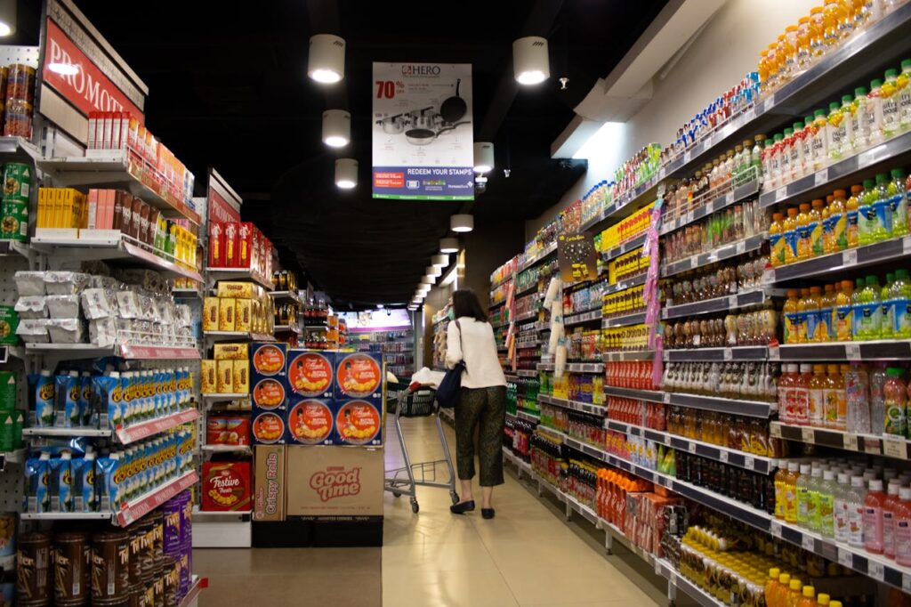 Woman pushing a cart down a supermarket aisle filled with promotional items and beverages