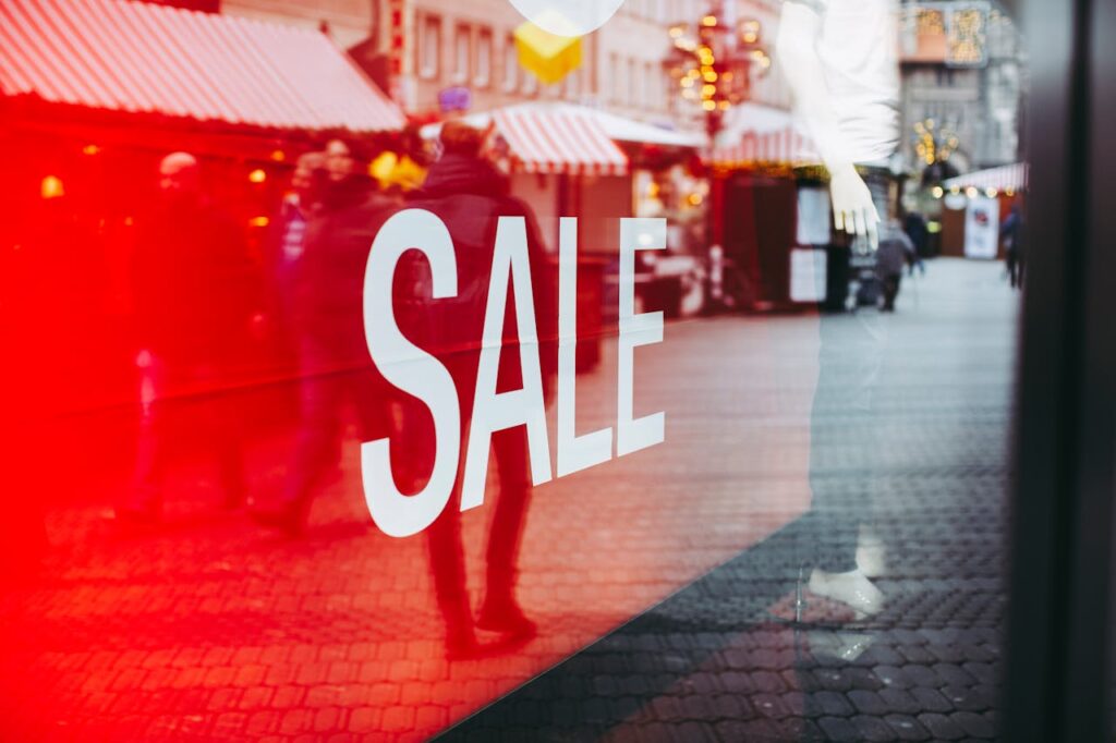 White “SALE” sign displayed on a red storefront window during a holiday shopping season