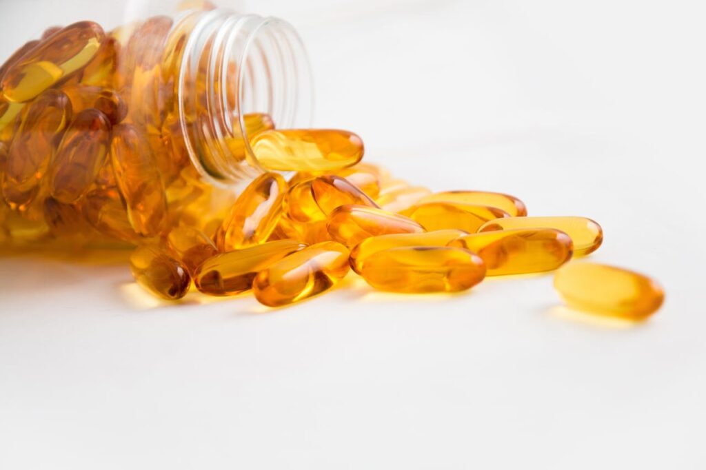 Amber-colored softgel capsules spilling out of a transparent bottle on a white background